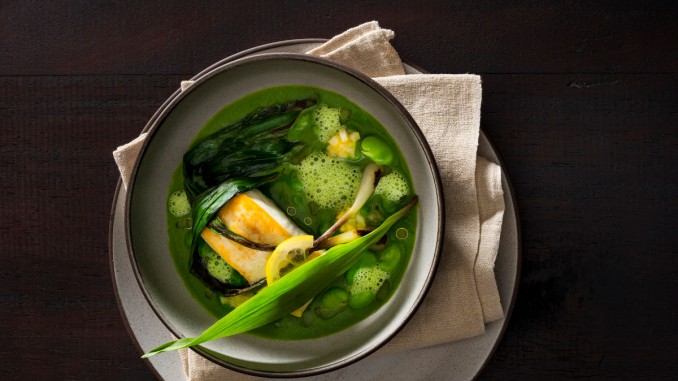 A bowl of green garlic broth with halibut, fava beans, charred ramps and finished with thinly sliced lemon, lemon relish, raw ramps and a drizzle of oil prepared by Chef/Owner Daniel Humm of NoMad